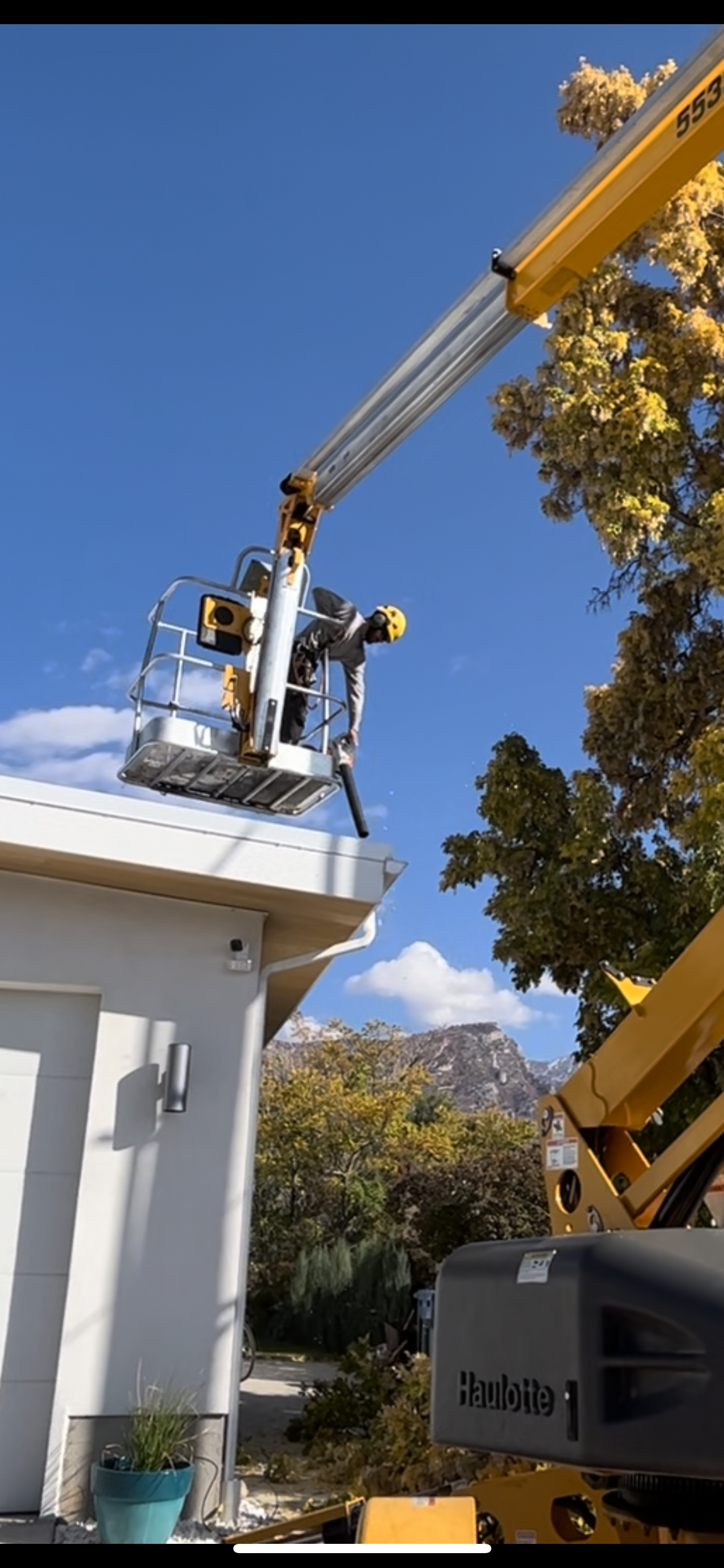 An arborist in a bucket lift trimming a tree, wearing a helmet and safety glasses